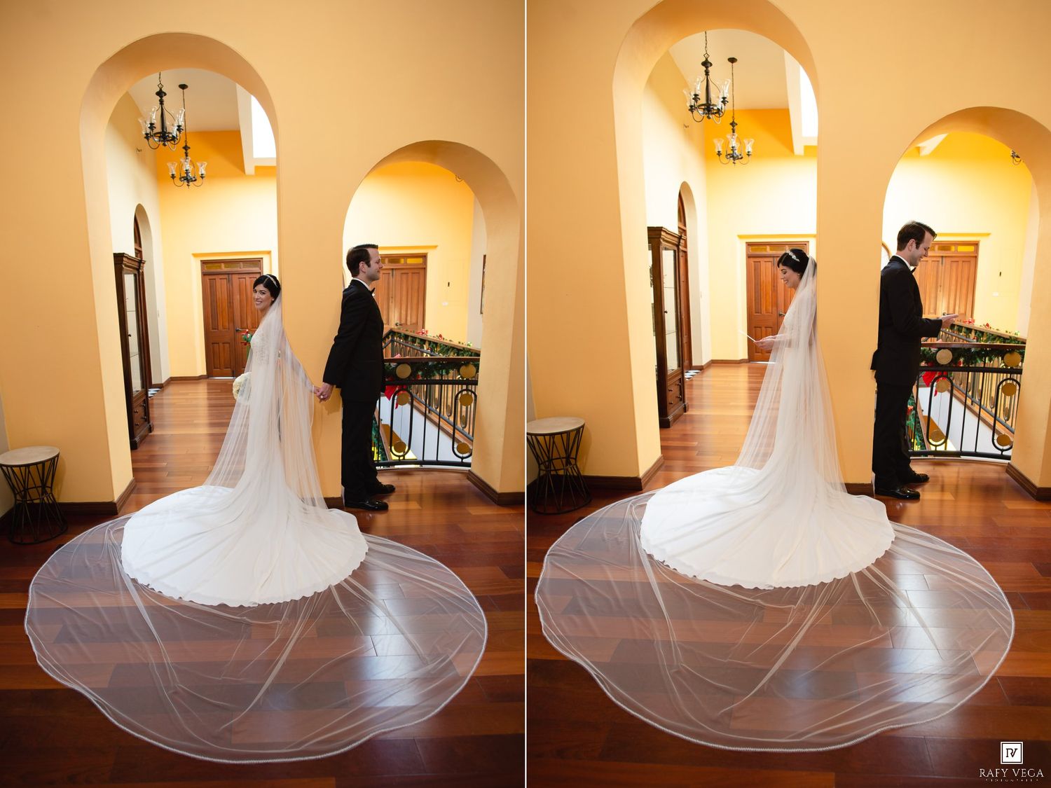 Bride in elegant white gown with long veil stands facing groom in black suit during indoor wedding first look.