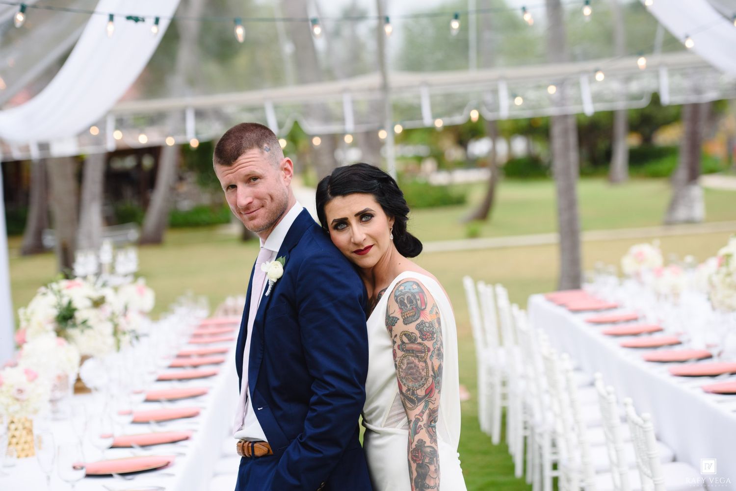 Bride and groom stand back-to-back smiling at outdoor wedding reception with elegant white draped tent.
