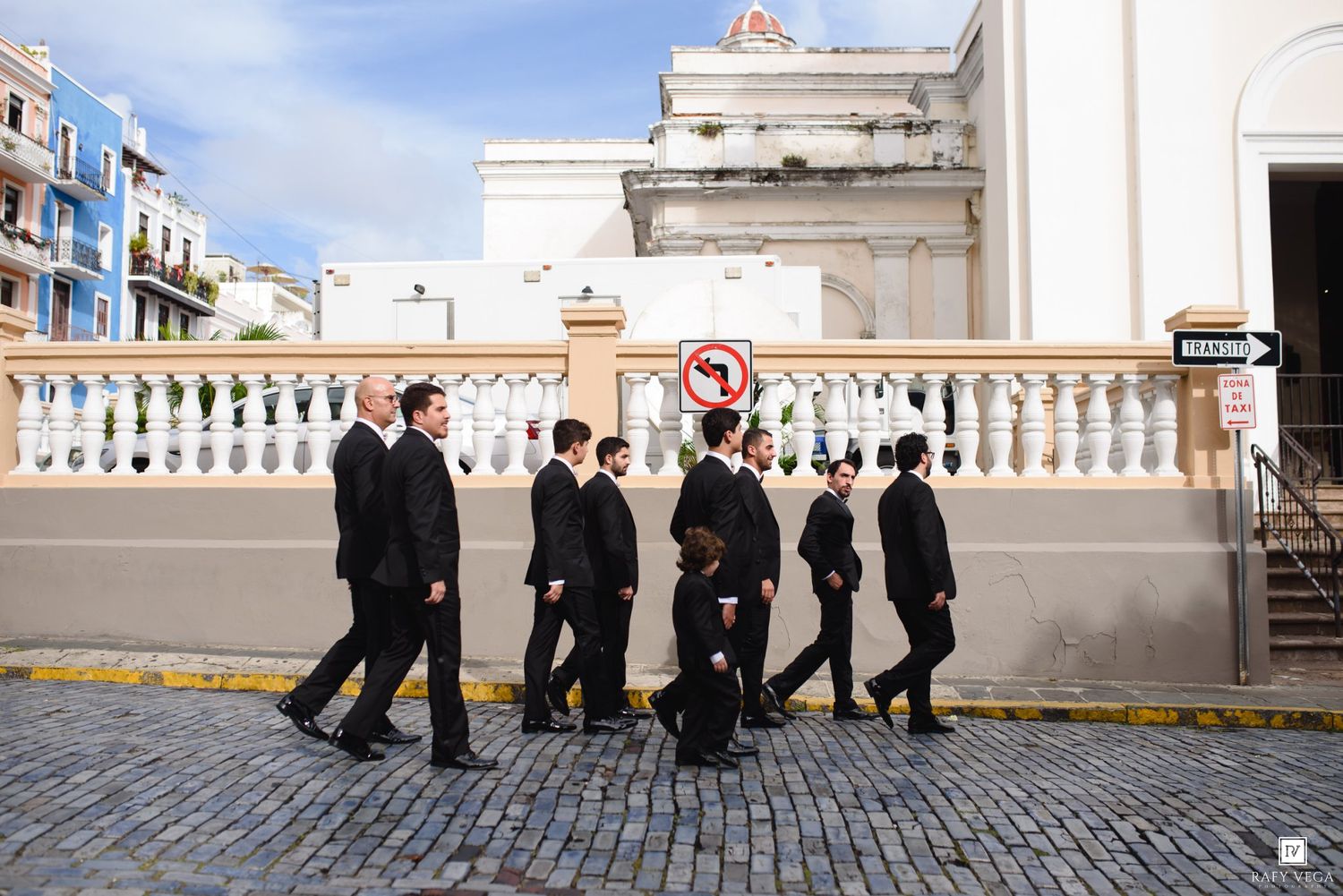 Group of people dressed in black formal attire walking along a cobblestone street in Old San Juan, Puerto Rico.