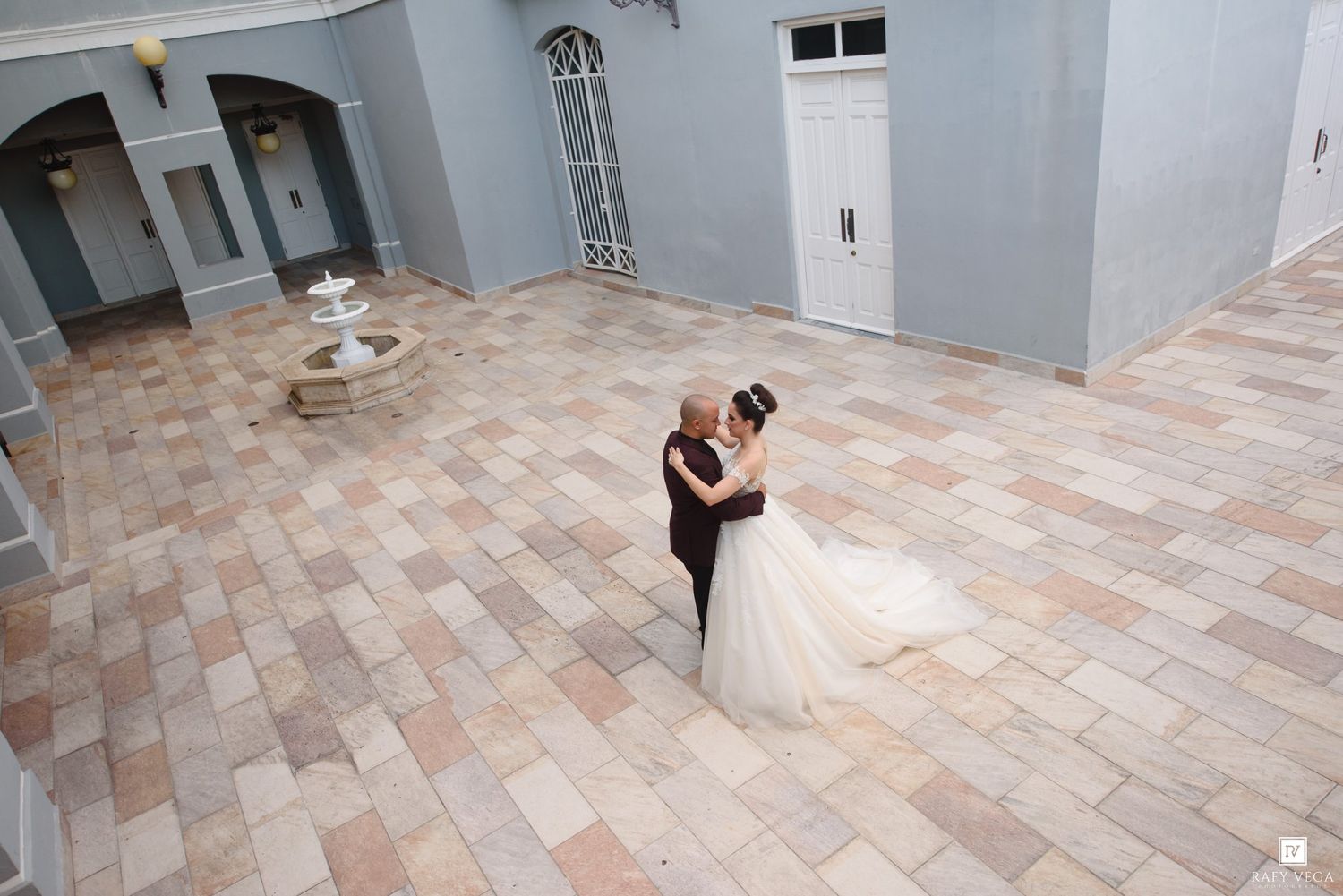 Bride and groom share first dance in elegant courtyard with fountain and blue walls on wedding day.