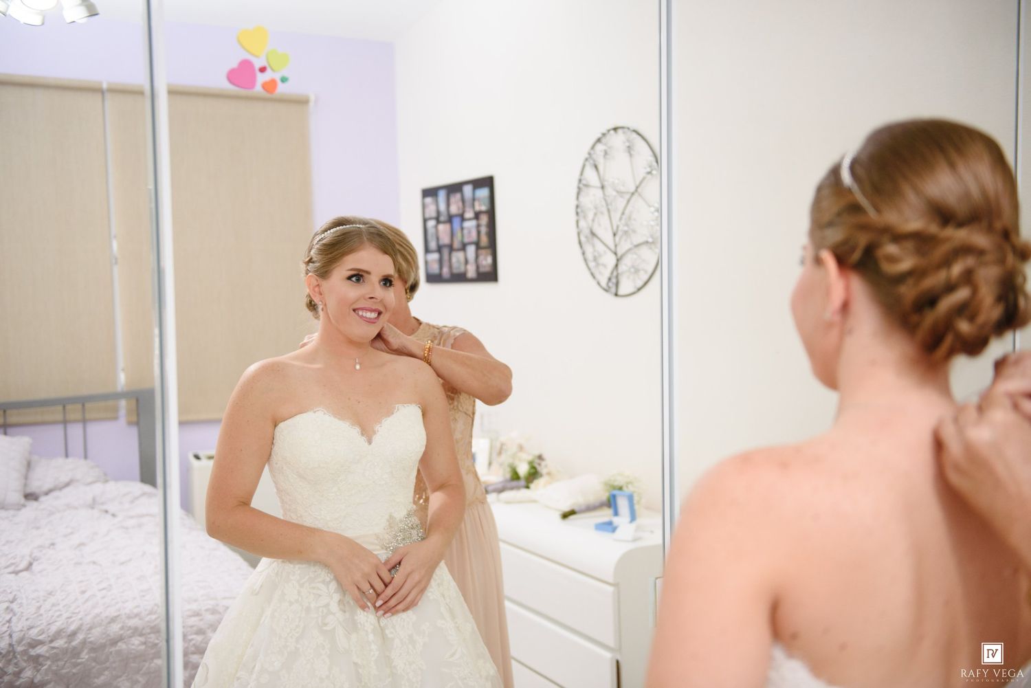 Bride in white lace wedding gown adjusting earring while looking in mirror during bridal preparations.