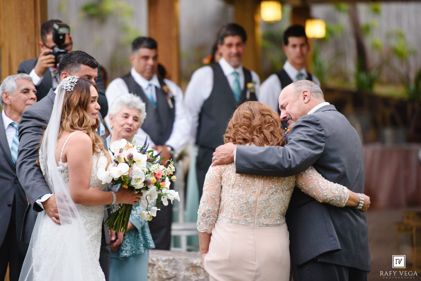 Emotional wedding moment as the groom embraces a family member while the bride holds her bouquet nearby.