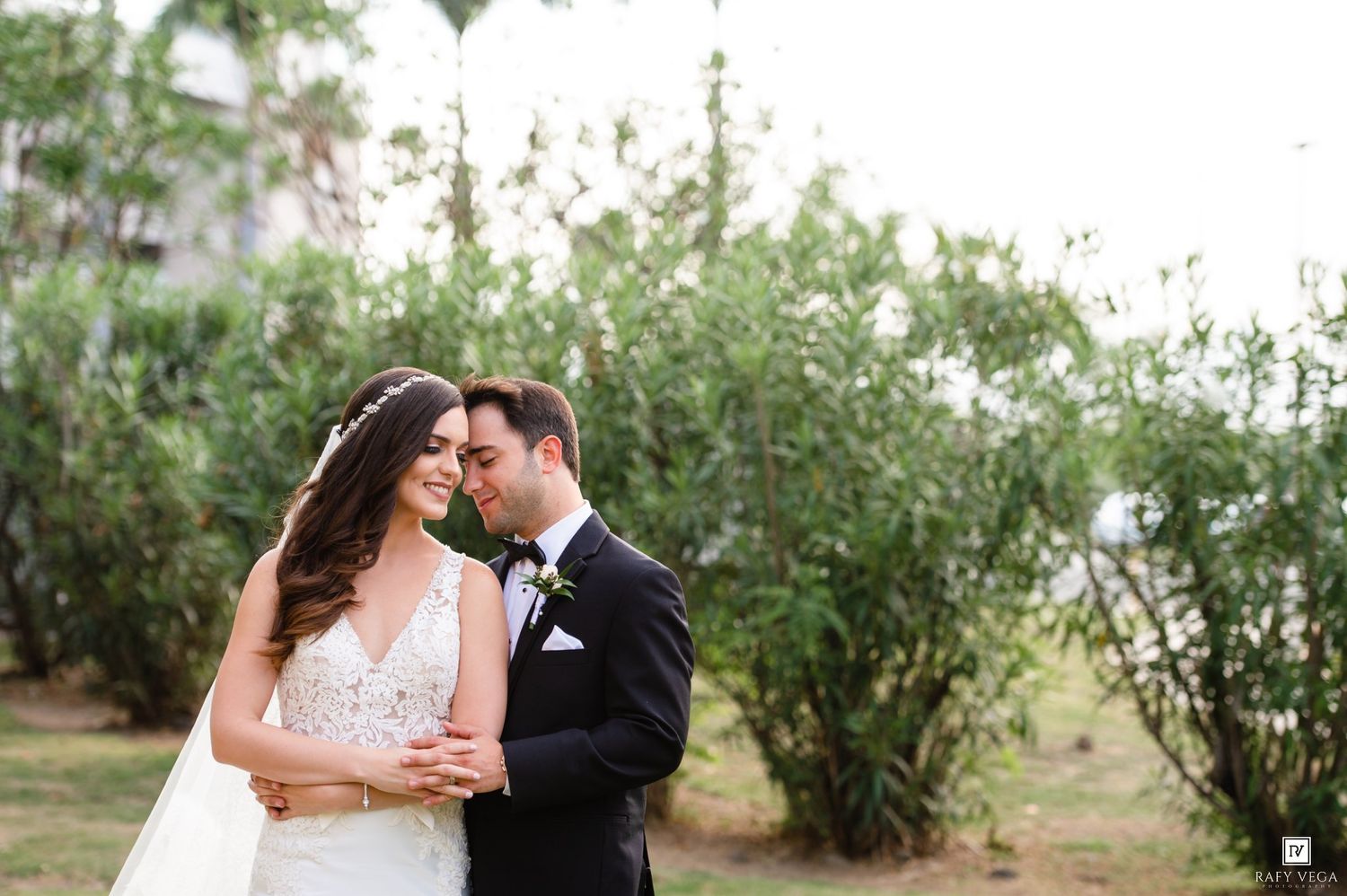 Bride and groom share romantic moment outdoors, touching foreheads tenderly in wedding attire.
