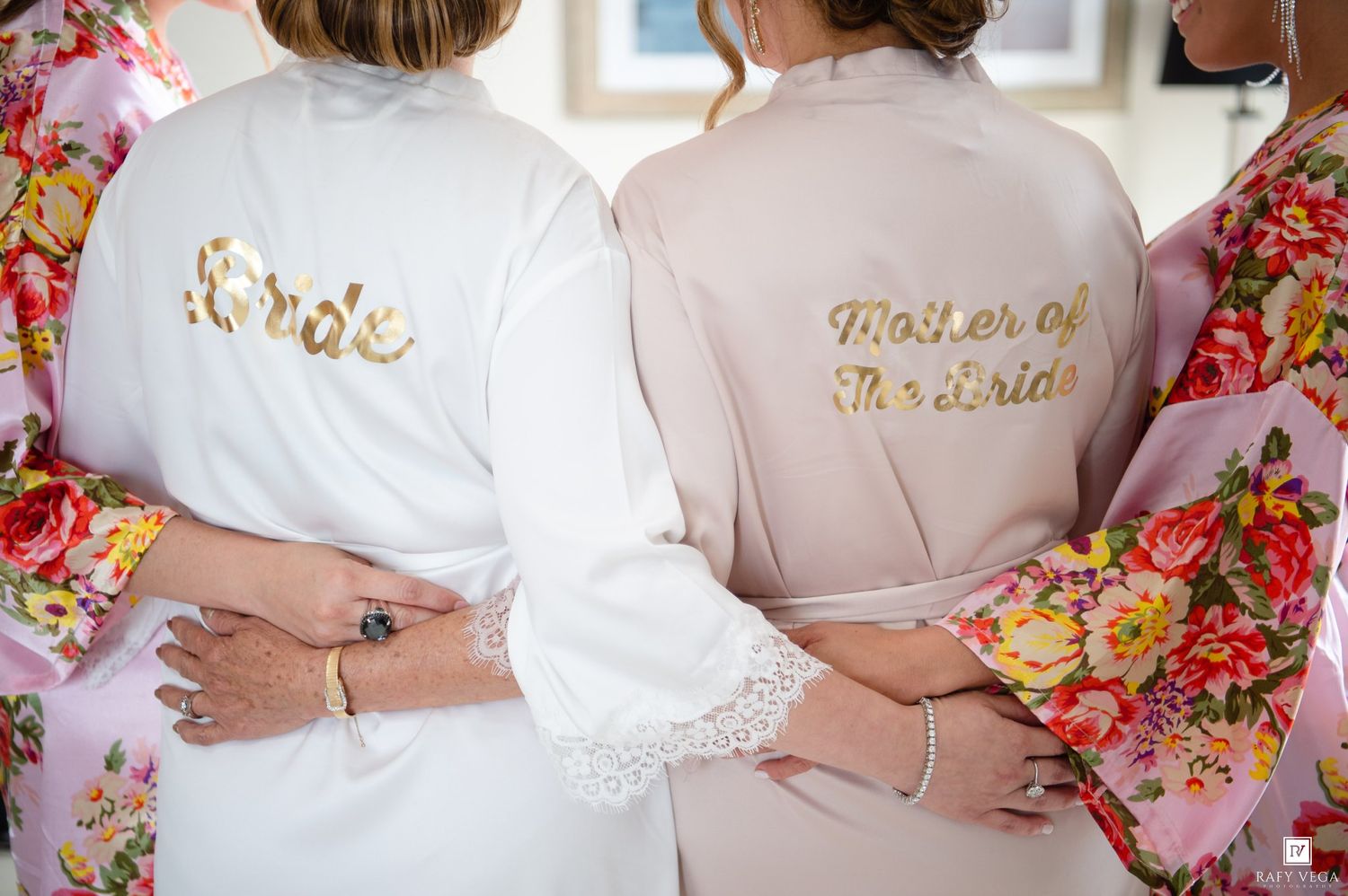 Bride and Mother of the Bride wearing matching satin robes with gold script lettering on wedding day.