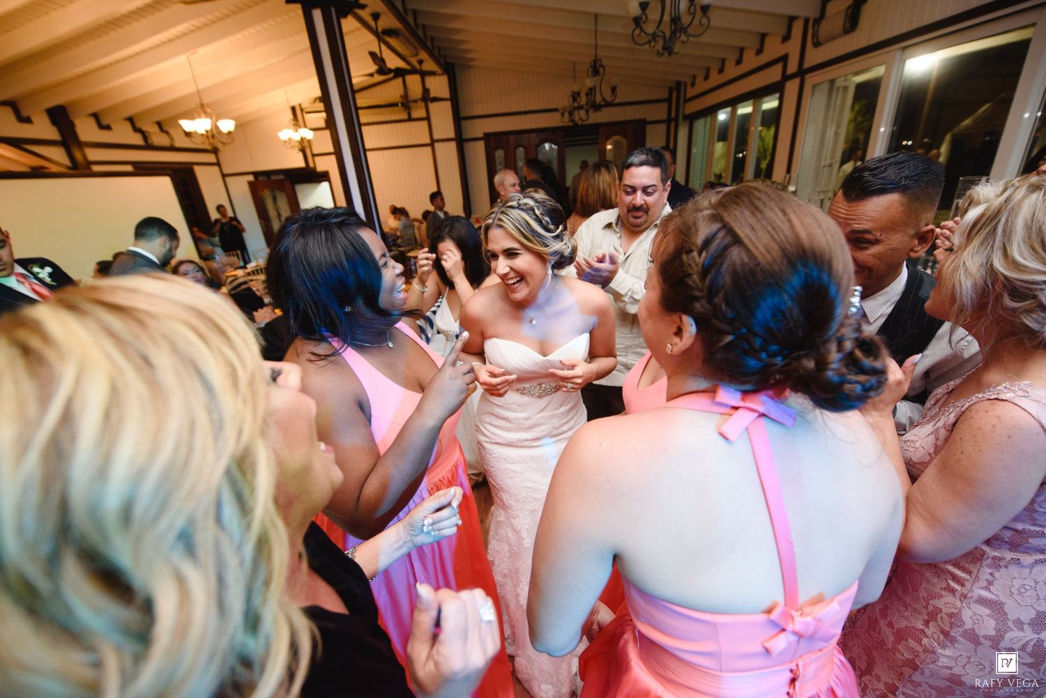 Bride surrounded by bridesmaids in pink dresses celebrating on the dance floor at a wedding reception.