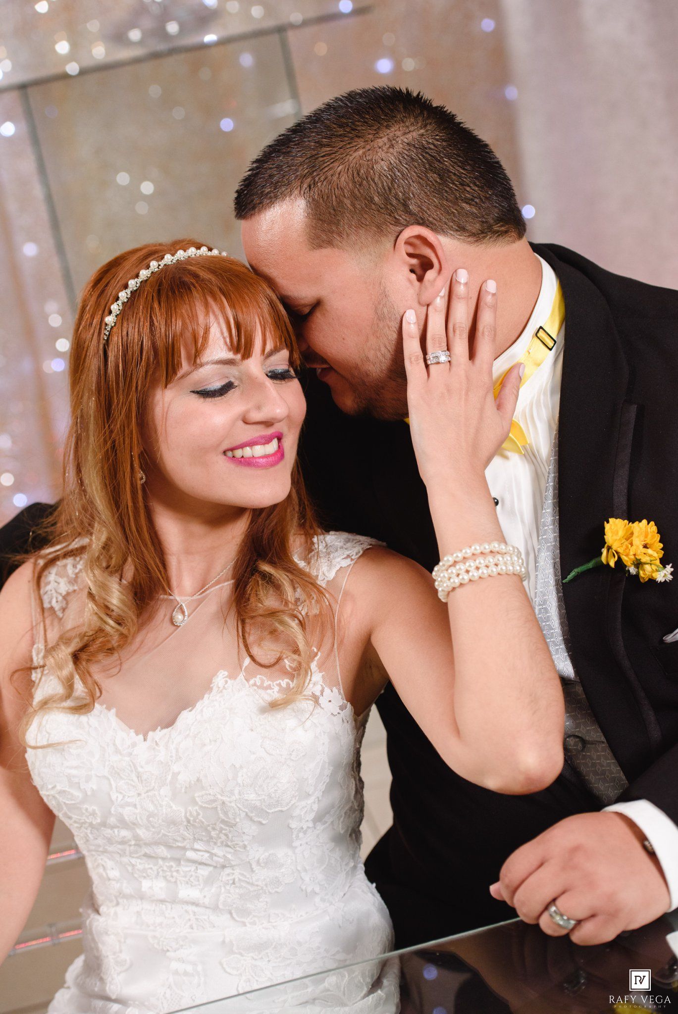 Bride and groom share an intimate moment cutting wedding cake, bride wearing lace dress and pearl bracelet.
