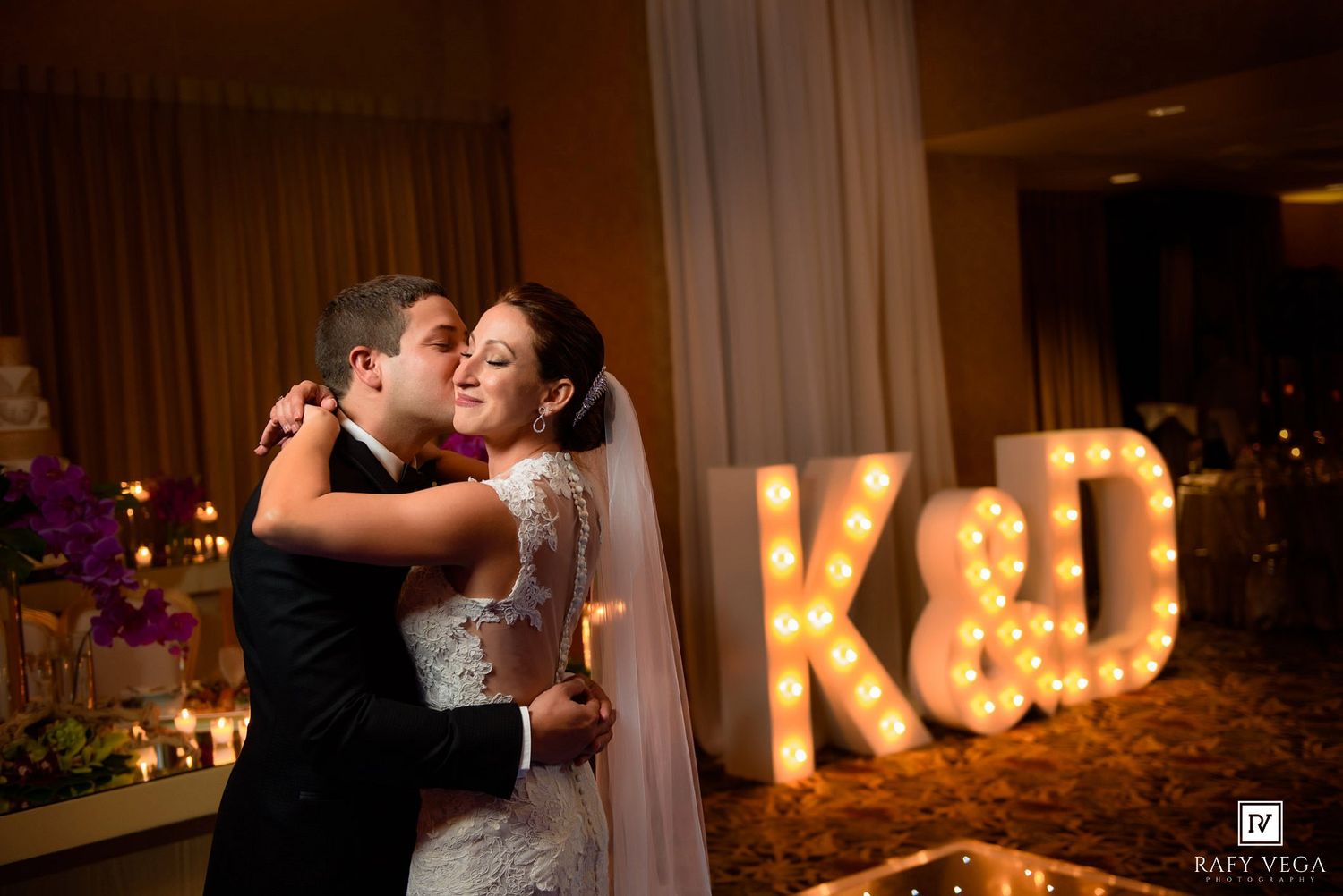 Bride and groom share first dance near illuminated K&D marquee letters at elegant wedding reception.