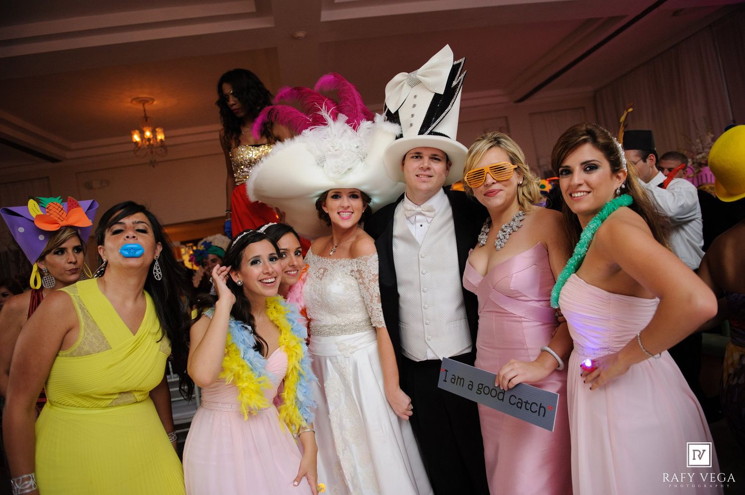 Wedding guests pose with fun props and colorful costumes at a lively wedding reception photo booth.