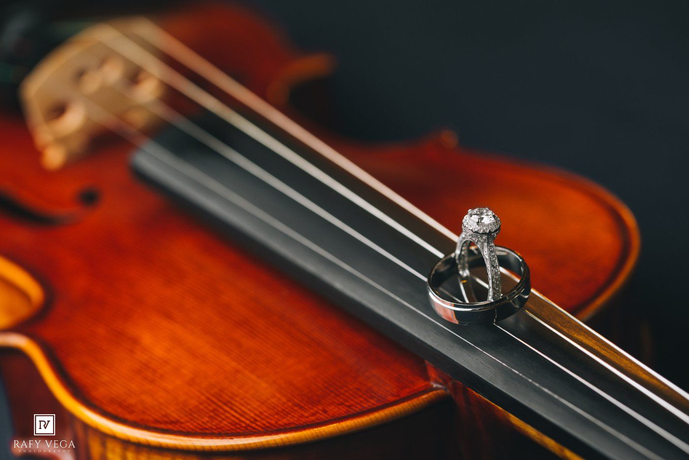 Diamond engagement ring resting on violin strings over a warm wooden body, elegant wedding detail photography.