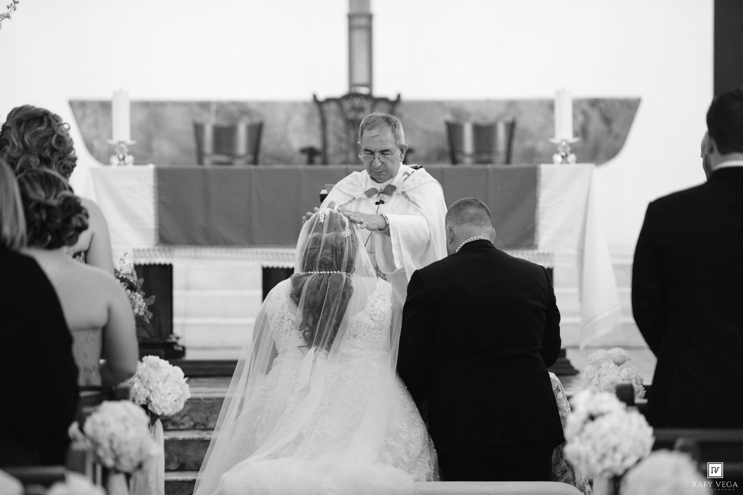 Black and white photo of a bride and groom kneeling at the altar during a church wedding ceremony.