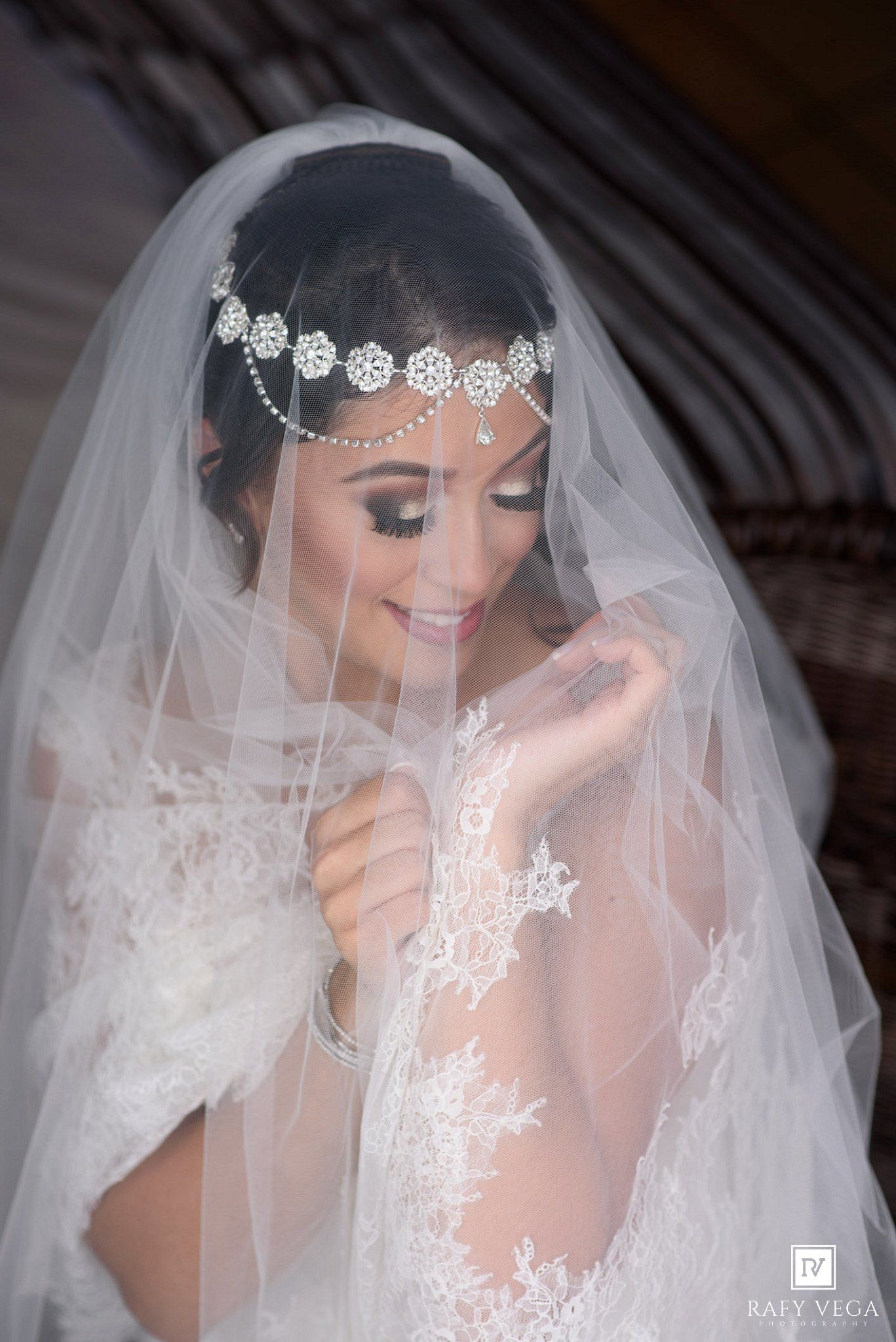Bride in white lace gown and veil with crystal headpiece smiles softly on her wedding day.