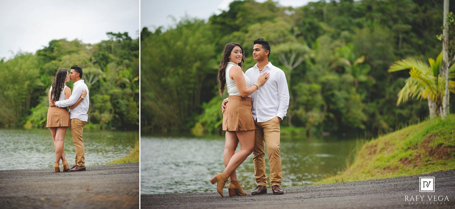 Couple poses romantically by a serene lake surrounded by lush tropical greenery during an outdoor engagement photo session.