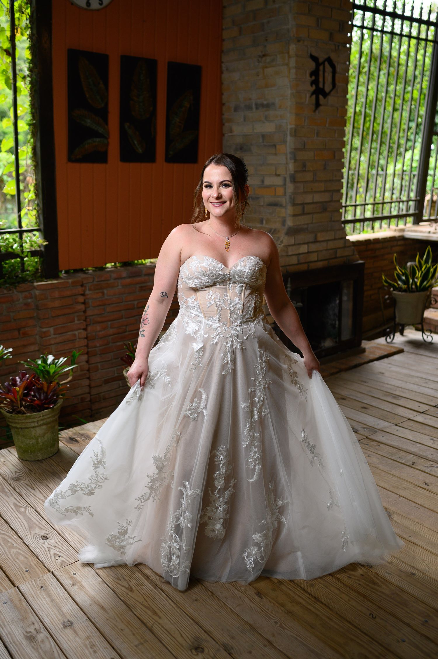 Bride in strapless lace ball gown wedding dress standing on wooden deck at outdoor venue.