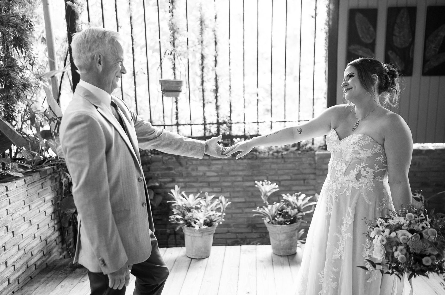 Black and white photo of a bride and groom reaching for each other's hands outdoors at a wedding ceremony.