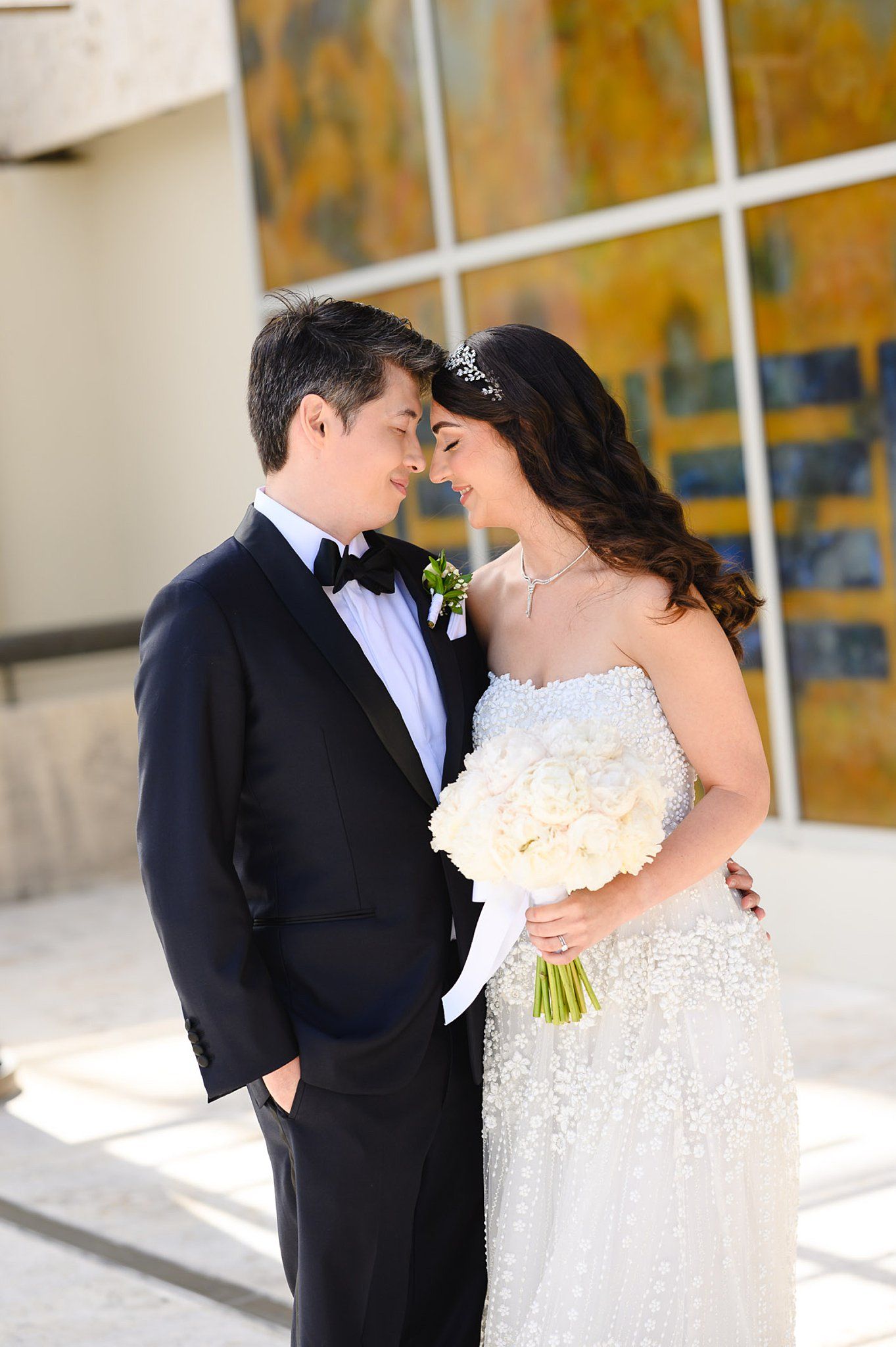 Bride and groom in formal wedding attire share an intimate moment outdoors, bride holding white hydrangea bouquet.
