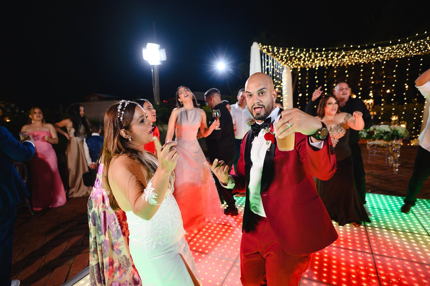 Bride and groom dancing joyfully on a colorful LED dance floor at an elegant outdoor wedding reception.