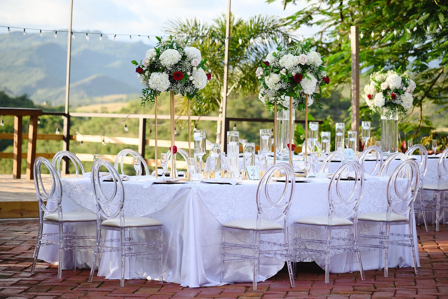 Elegant outdoor wedding reception with white tablecloths, ghost chairs, and floral centerpieces set against a mountain backdrop.