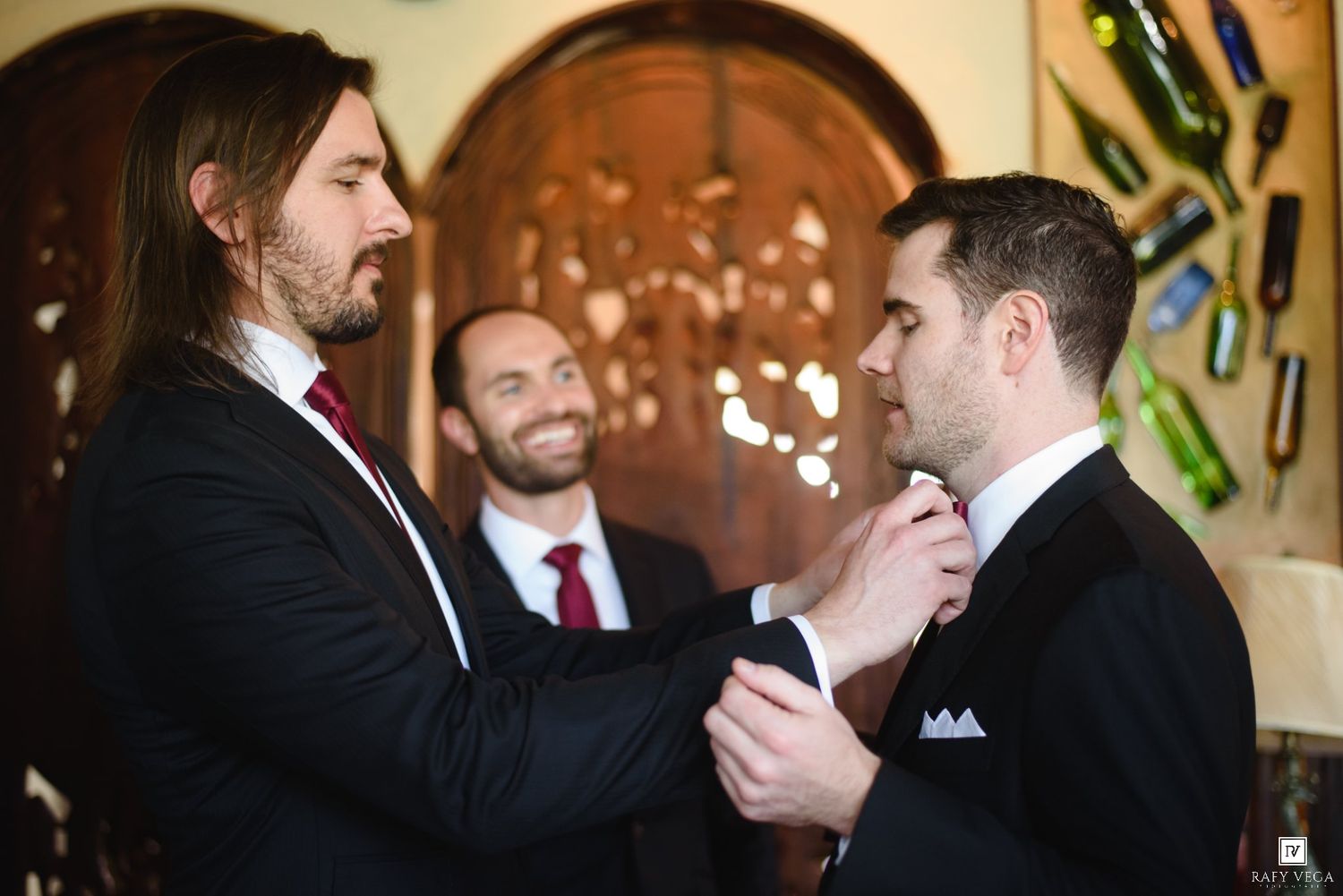 Groomsmen helping groom adjust his tie before wedding ceremony in elegant venue.
