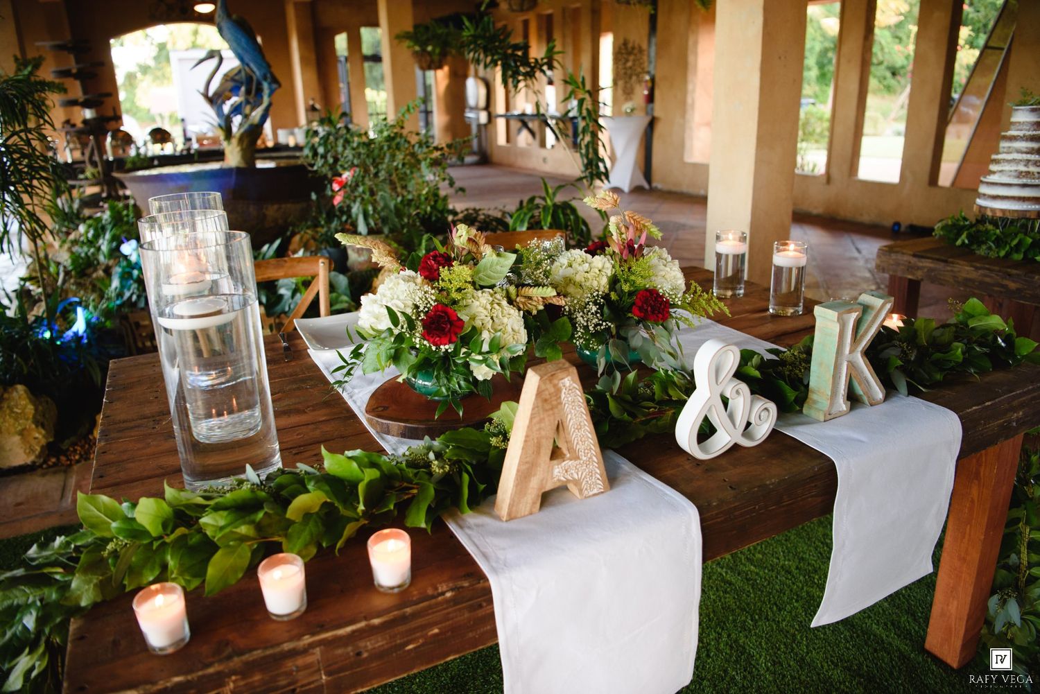 Elegant wedding sweetheart table with floral centerpiece, wooden letter decorations, candles, and greenery garland.