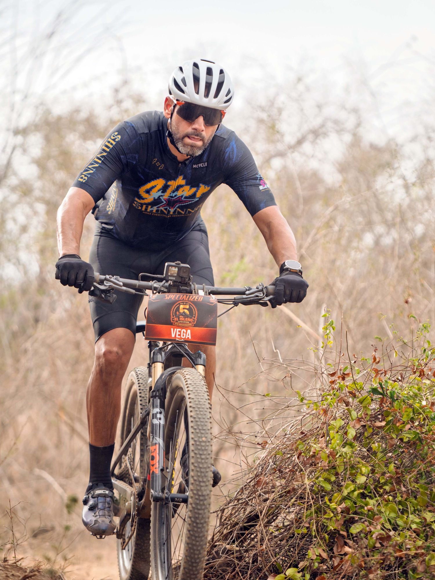 Man in cycling gear rides a mountain bike on a rugged dirt trail wearing a white helmet and dark jersey.