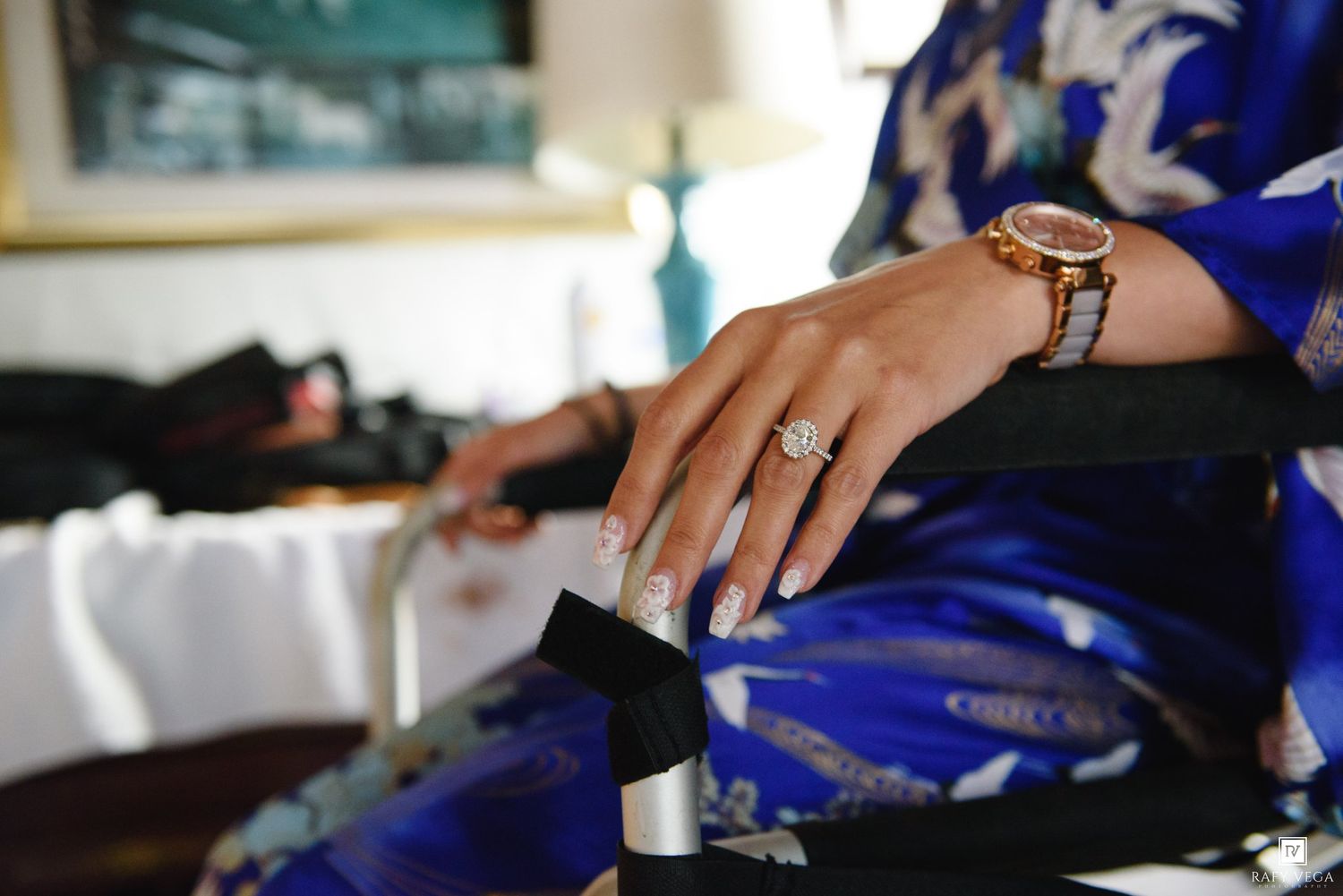 Woman in blue floral kimono displaying diamond engagement ring and gold watch on her hand.