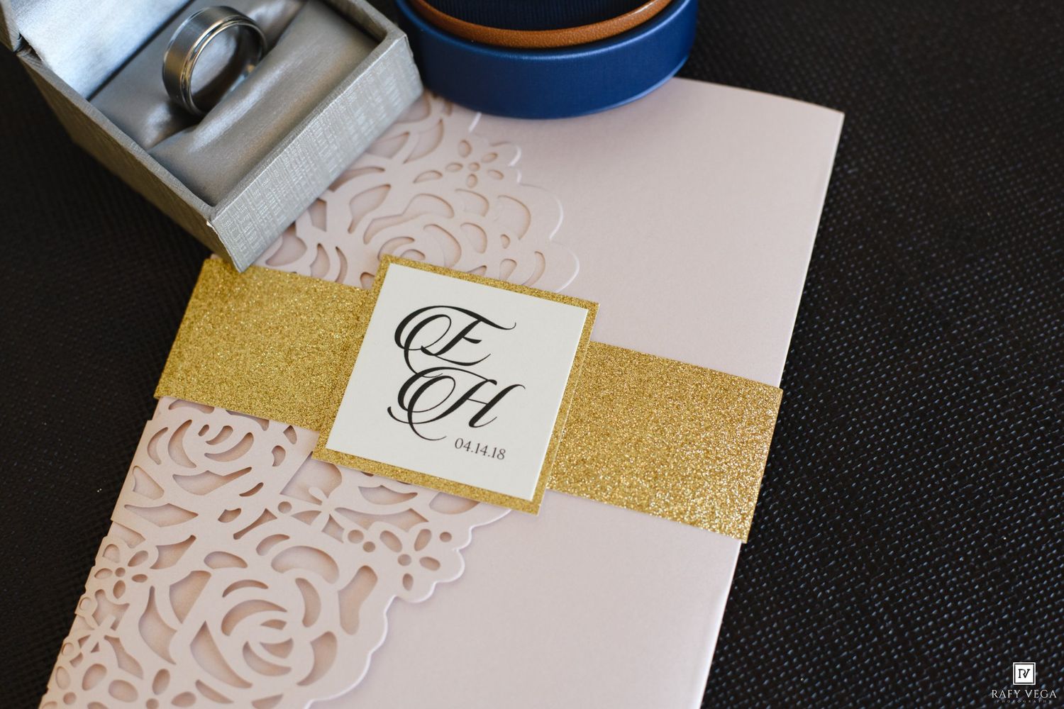 Elegant pink laser-cut wedding invitation with gold glitter band and monogram initials on white card.