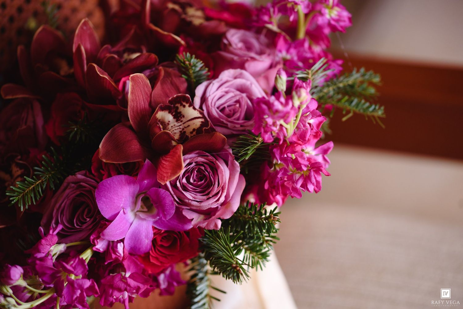 Lush bouquet of deep magenta roses, purple orchids, and fuchsia blooms with green foliage for a wedding.