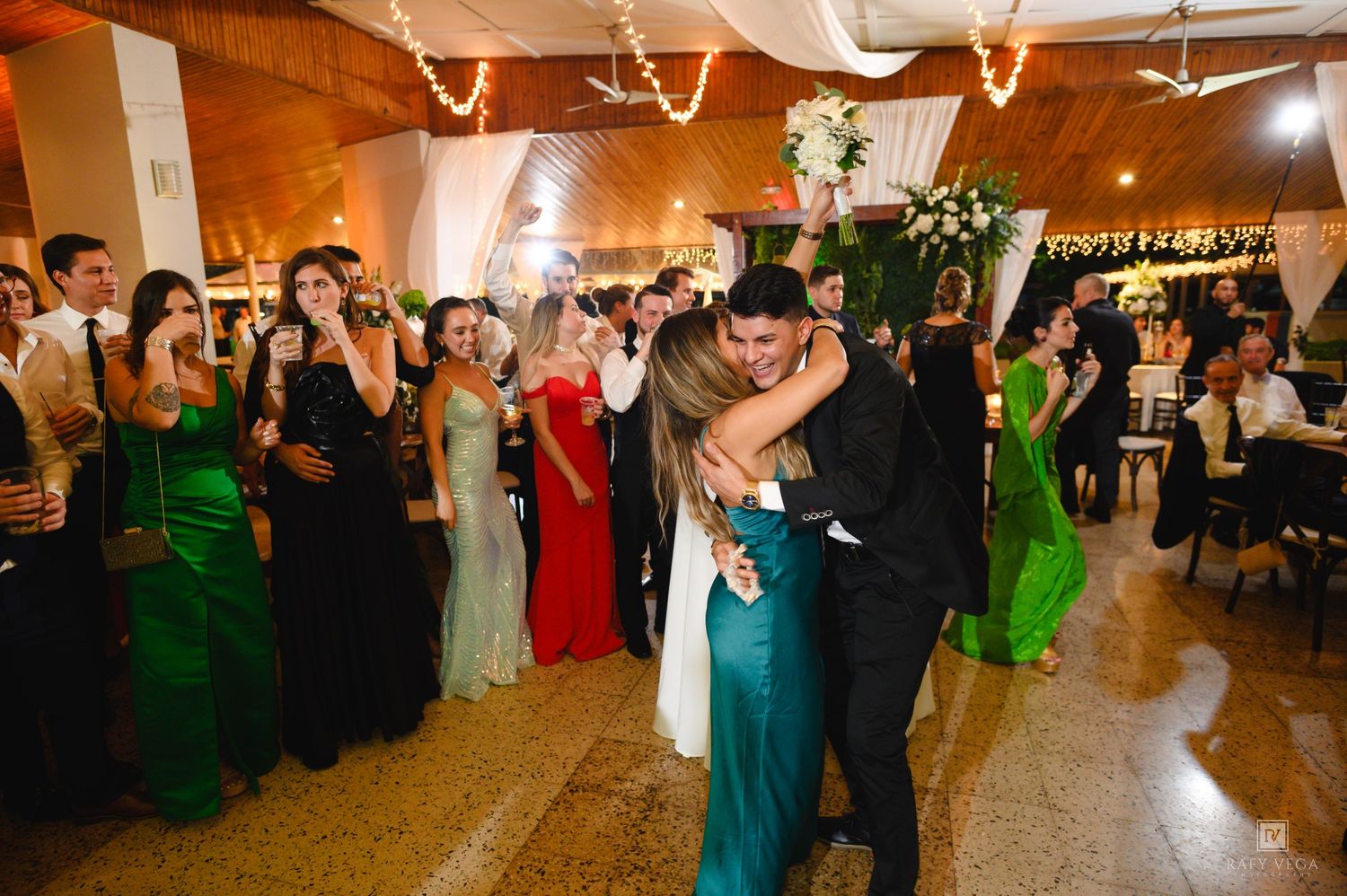 Couple shares first dance at wedding reception while guests in elegant green gowns and formal wear look on.