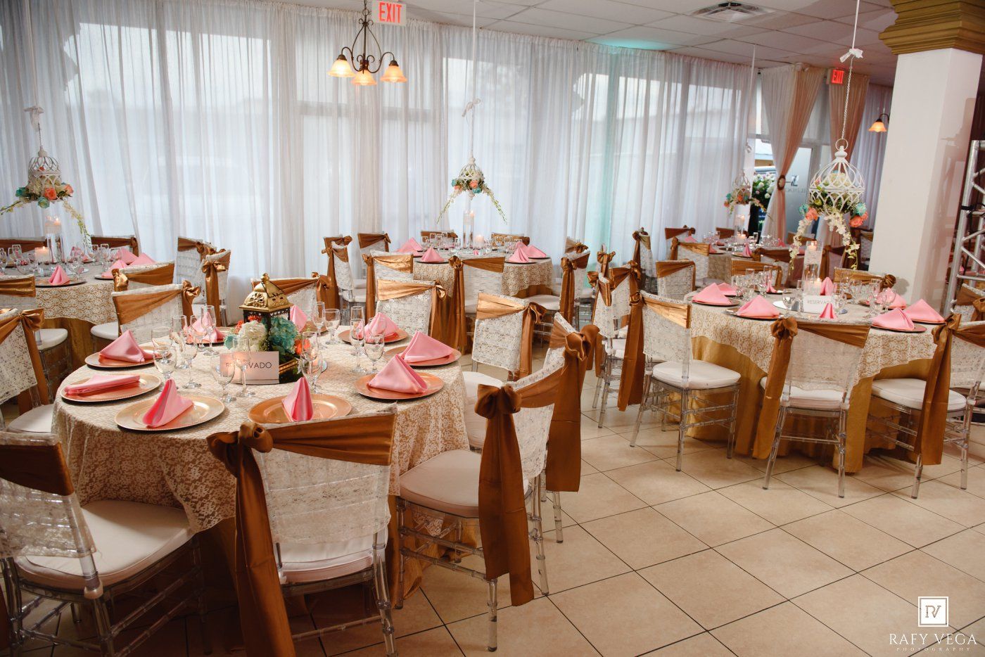 Elegant banquet hall with round tables set with pink napkins, floral centerpieces, and chiavari chairs for a wedding reception.
