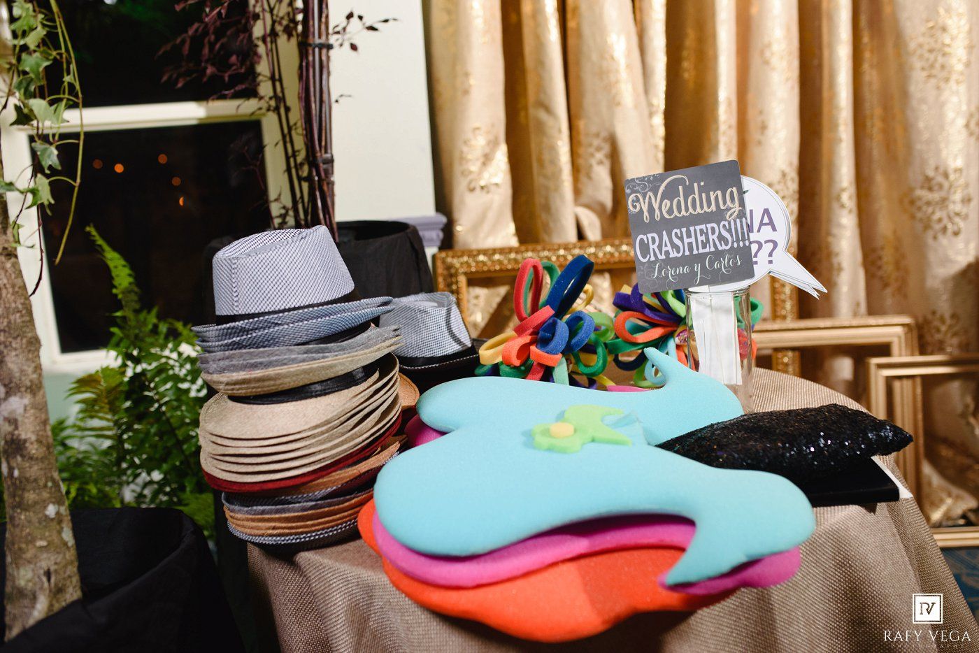Wedding photo booth props table with colorful hats, glasses, and a Wedding Crashers sign for guests.
