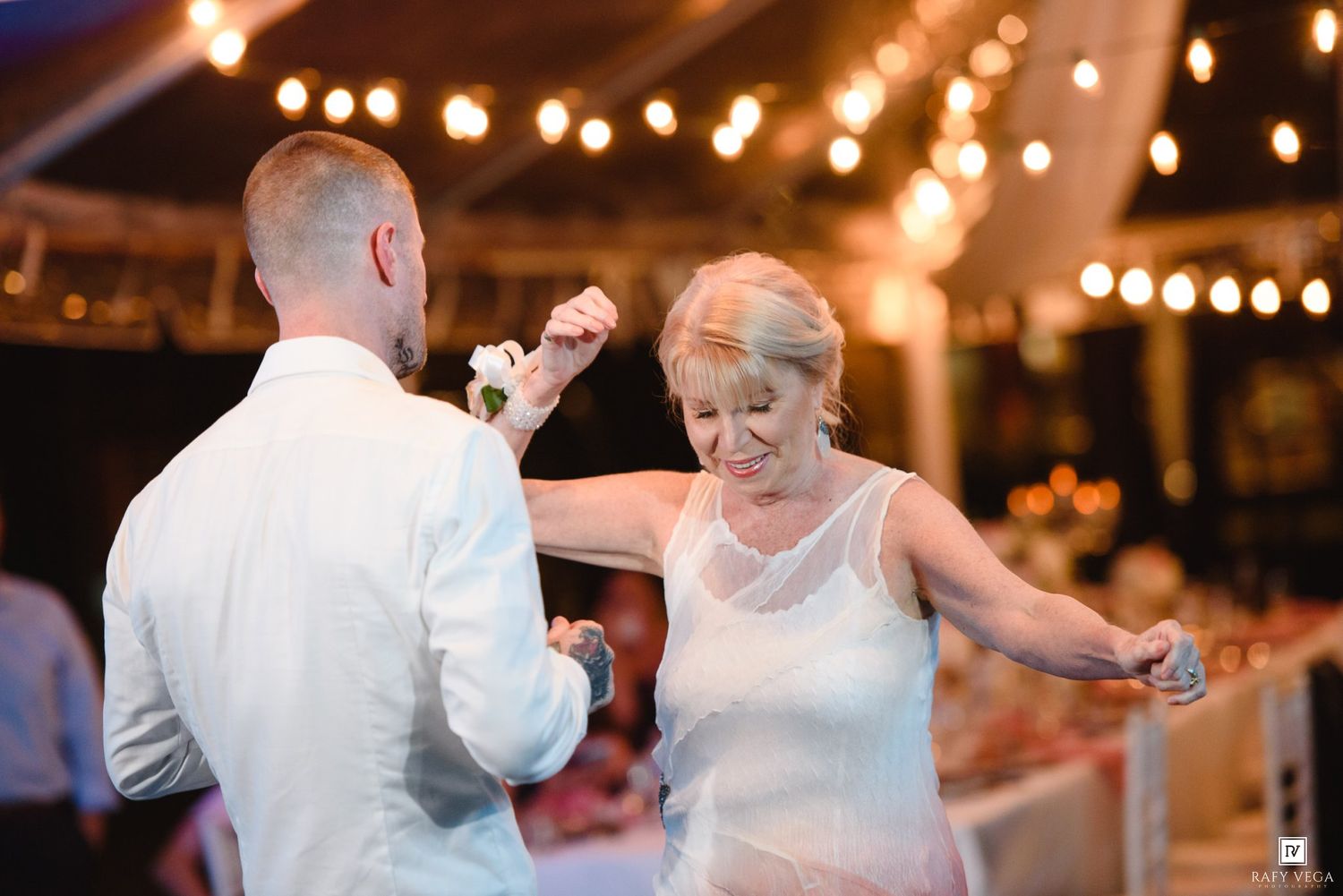 A couple shares a joyful dance under warm string lights at an elegant outdoor wedding reception.