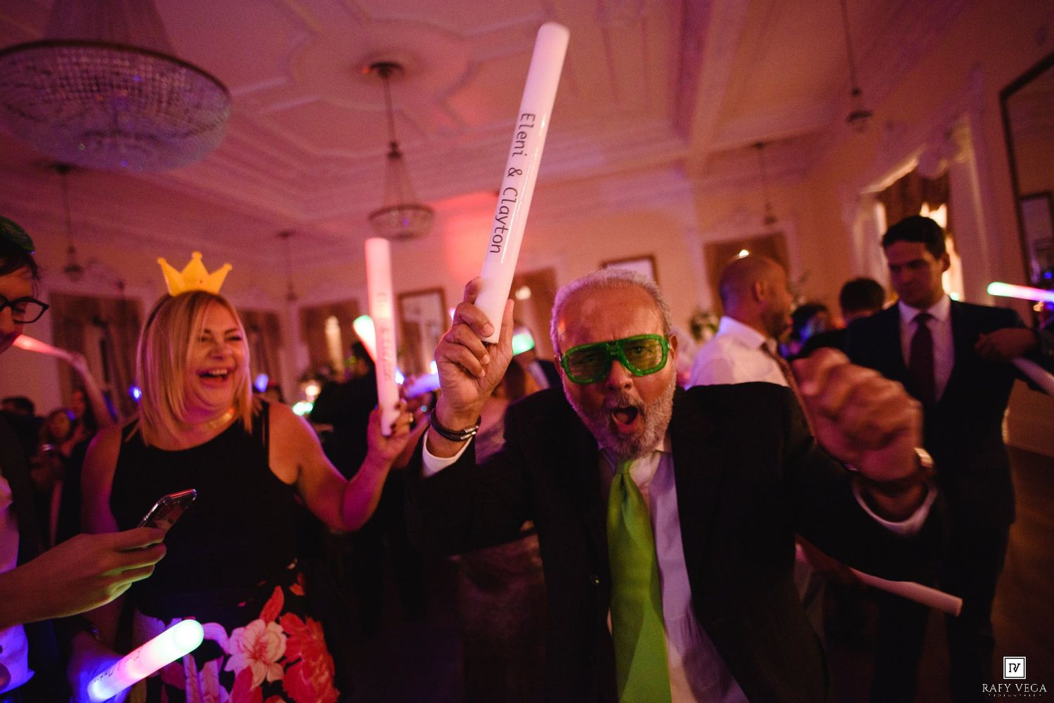 Guests dance joyfully with glow sticks and novelty glasses at a lively wedding party.