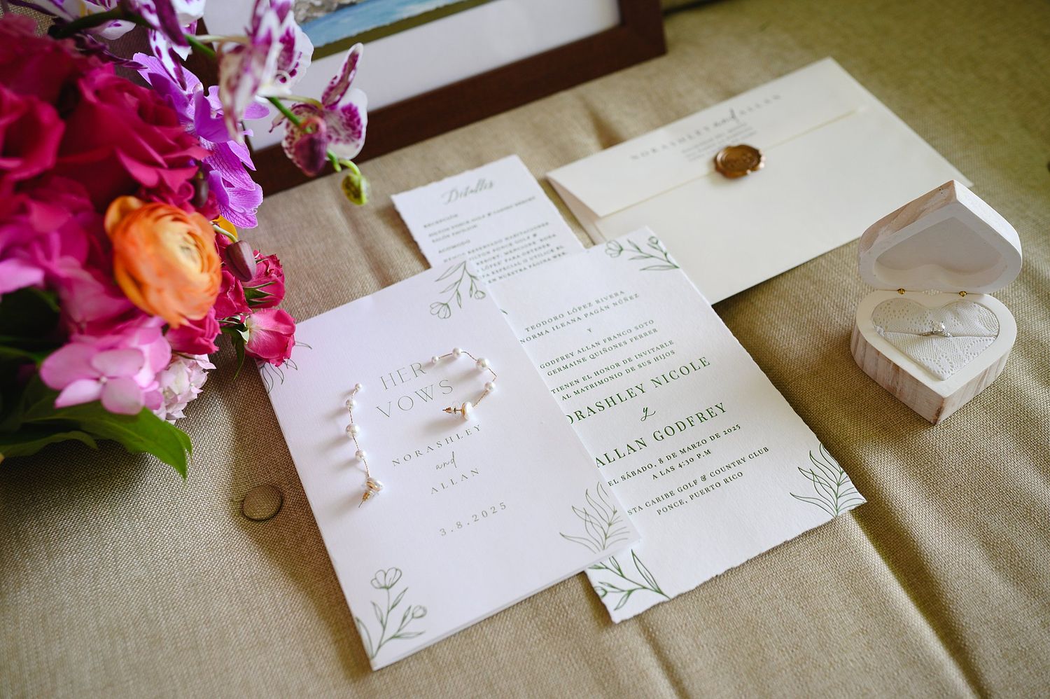 Elegant wedding invitation suite with floral accents, wax seal envelope, and rings on a neutral linen background.