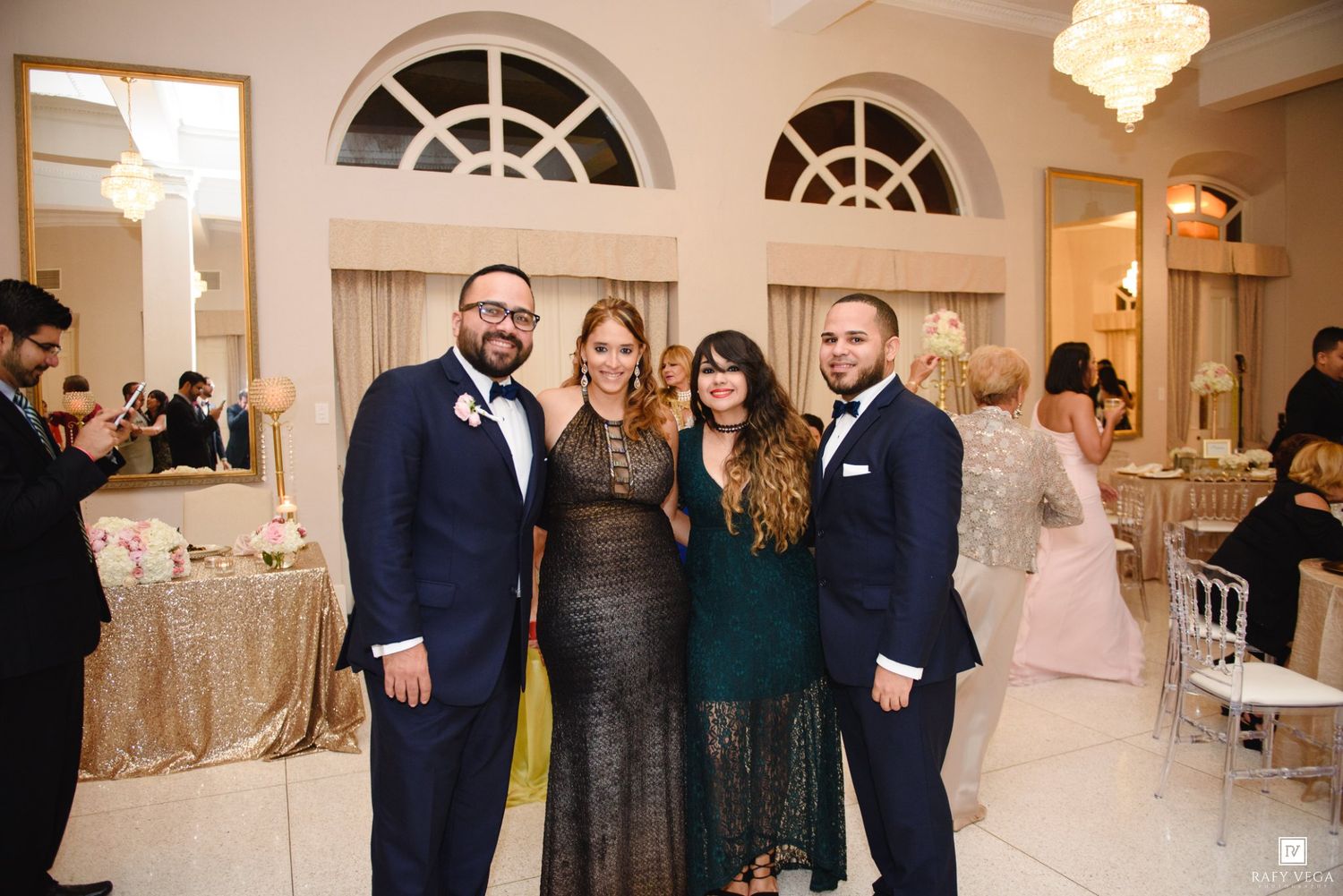 Four guests posing together smiling at elegant wedding reception venue with chandeliers.