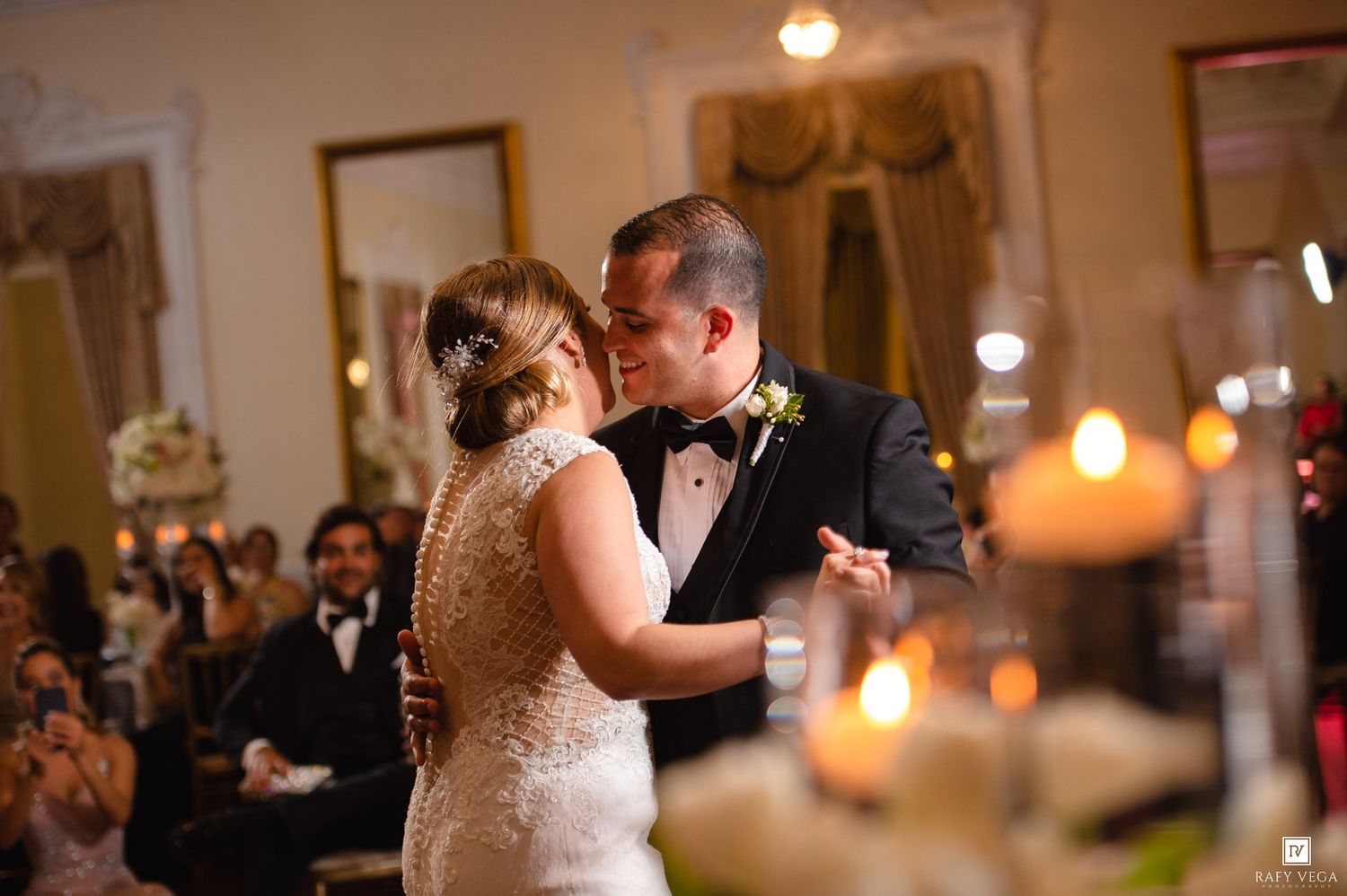 Bride and groom share their first dance surrounded by candlelight at elegant wedding reception.