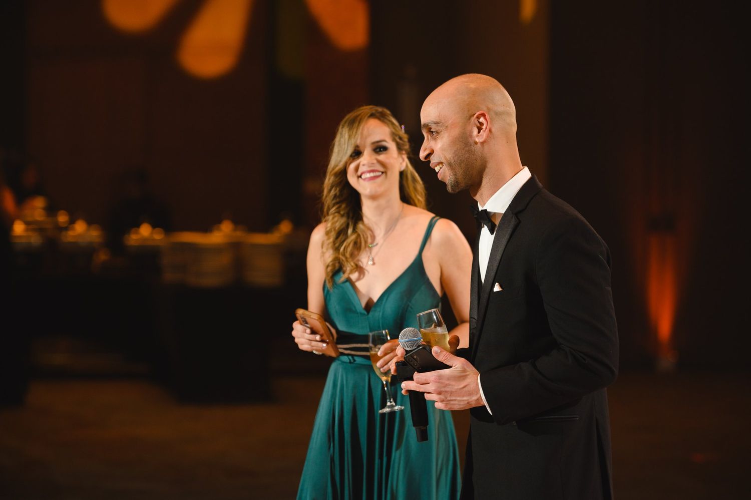 Elegant couple in formal attire toasting with champagne at a gala event, woman in teal gown, man in black tuxedo.