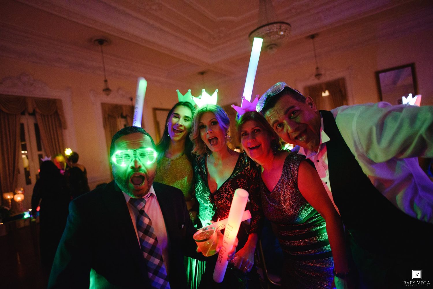 Group of friends posing with glowing neon light sticks and masks at a festive party celebration.