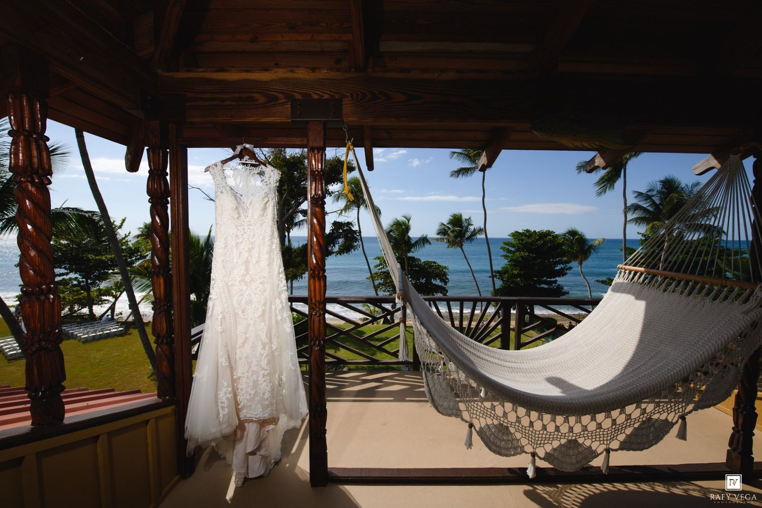 White lace wedding dress hanging on a tropical beachfront porch with a hammock and ocean view.