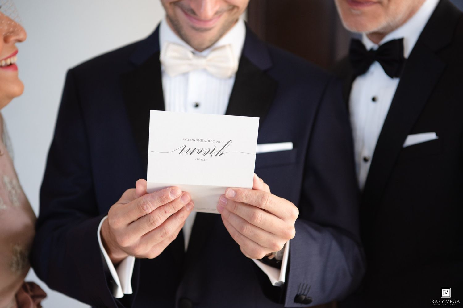 Groom in tuxedo holding elegant white wedding vow booklet with calligraphy script at ceremony.
