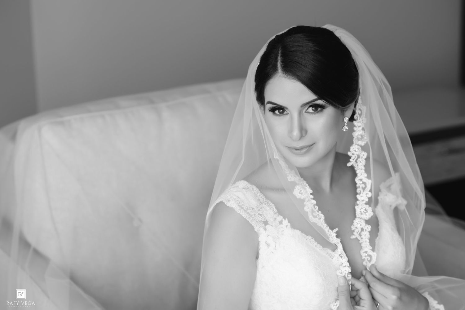 Black and white bridal portrait of a beautiful bride wearing a lace wedding dress and veil, seated elegantly.