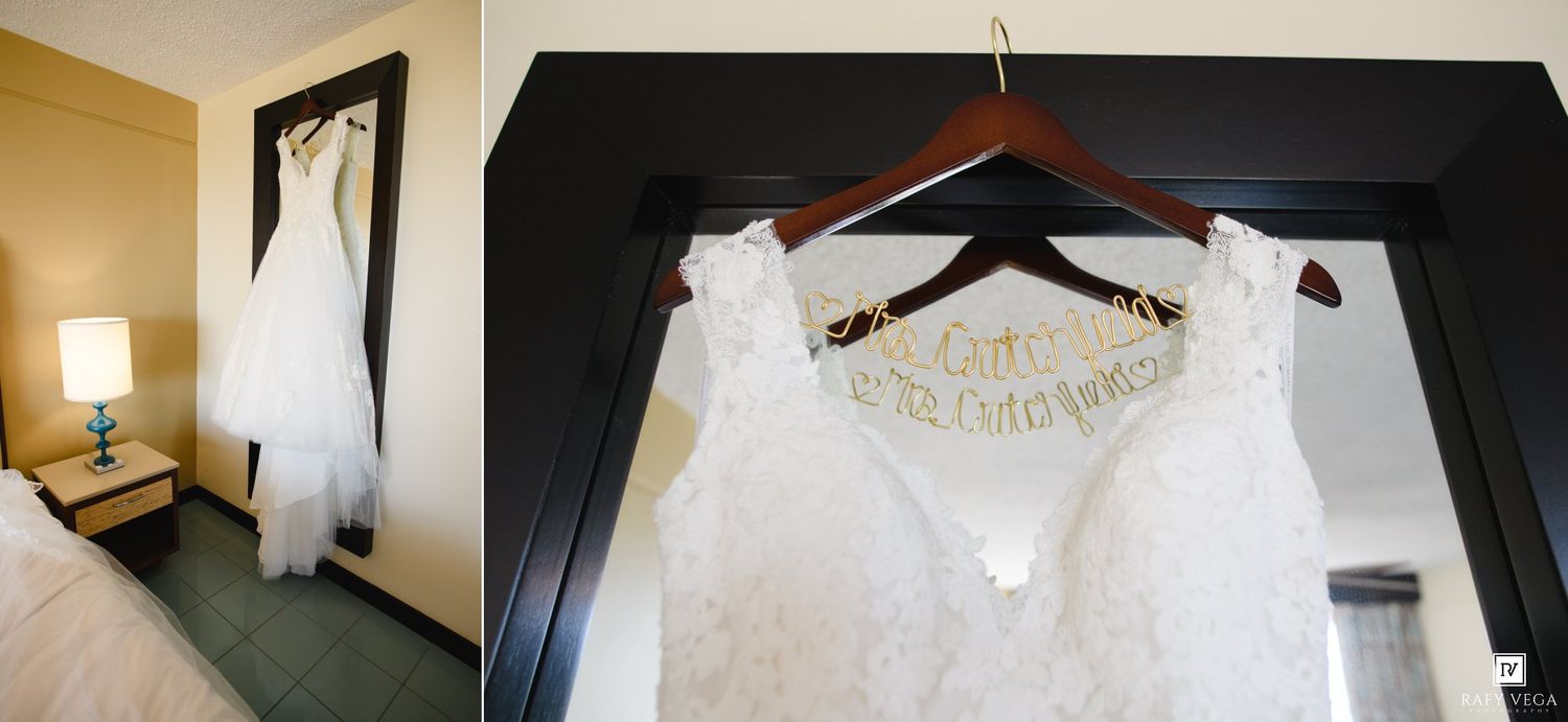 White wedding dress hanging in hotel room beside lace gown on personalized wooden hanger.
