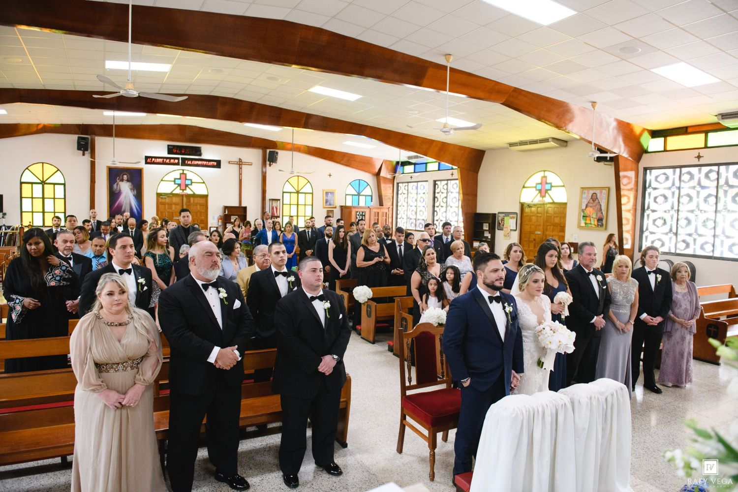 Wedding ceremony in a church with bride, groom, and wedding party at the altar, guests seated in pews.