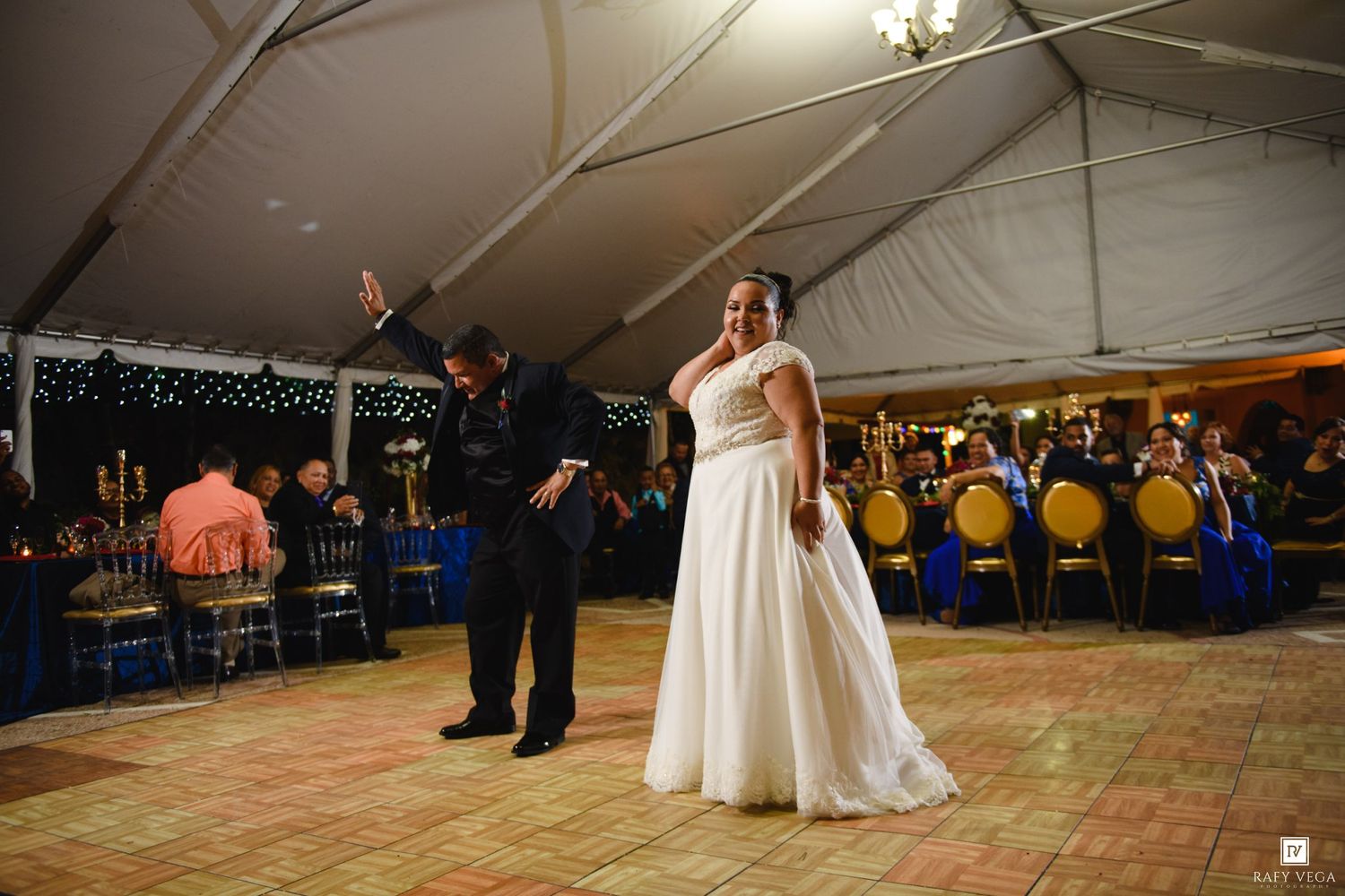 Bride and groom share their first dance under a white tent at an elegant wedding reception with blue and gold decor.