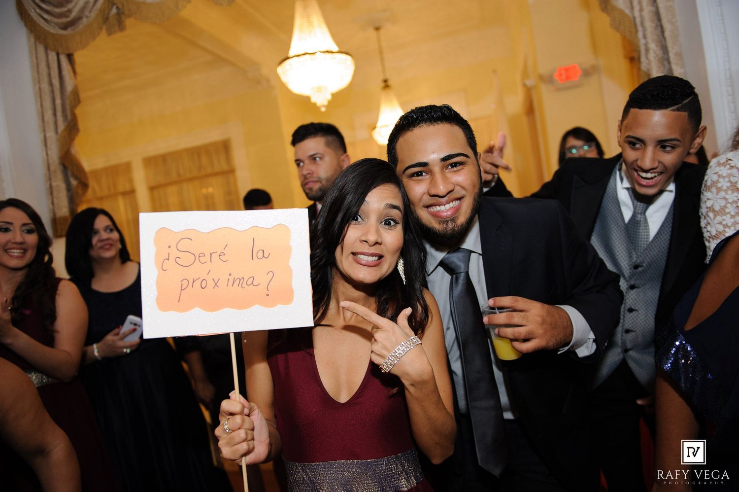 Couple posing with a handwritten sign at a formal wedding reception event.