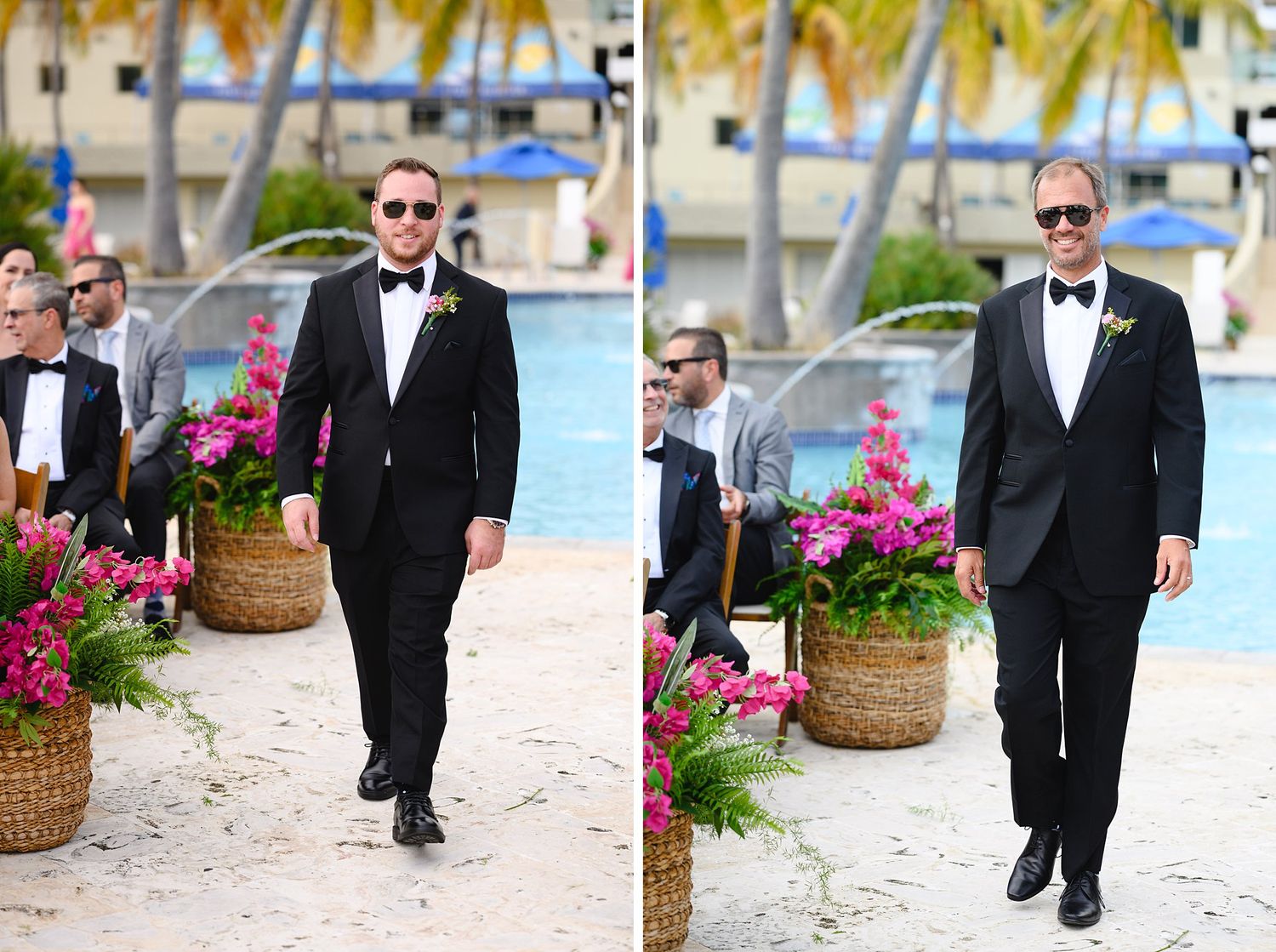 Two groomsmen in black tuxedos with bow ties walk along a poolside wedding aisle adorned with tropical pink flowers.
