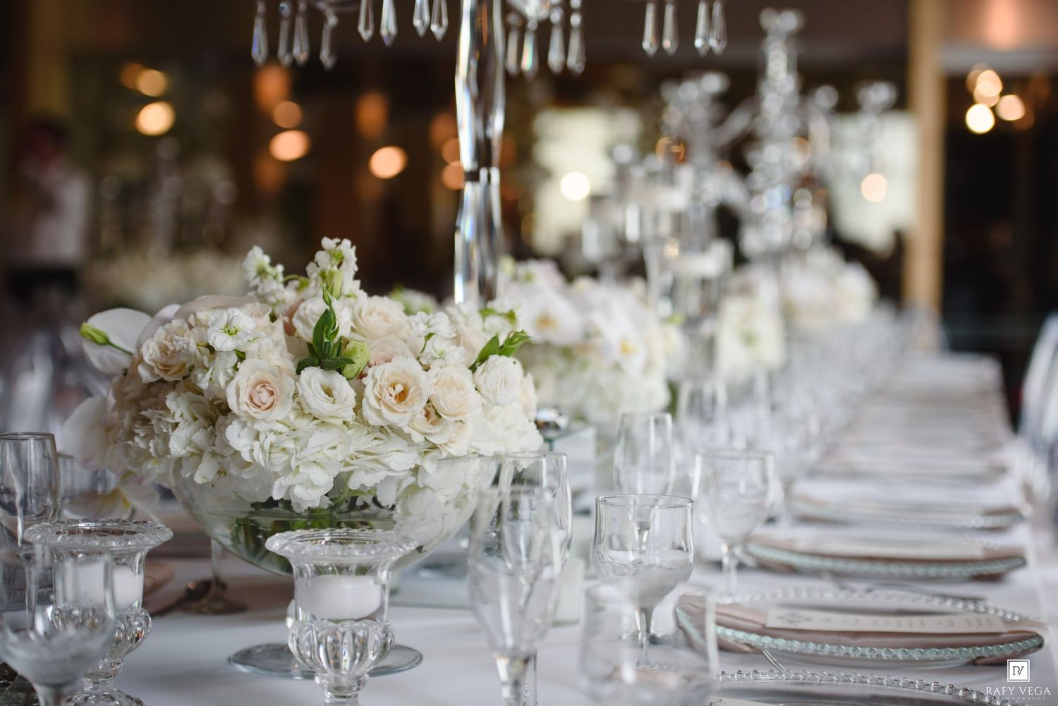 Elegant wedding reception table with white floral centerpieces, crystal candelabras, and fine place settings.