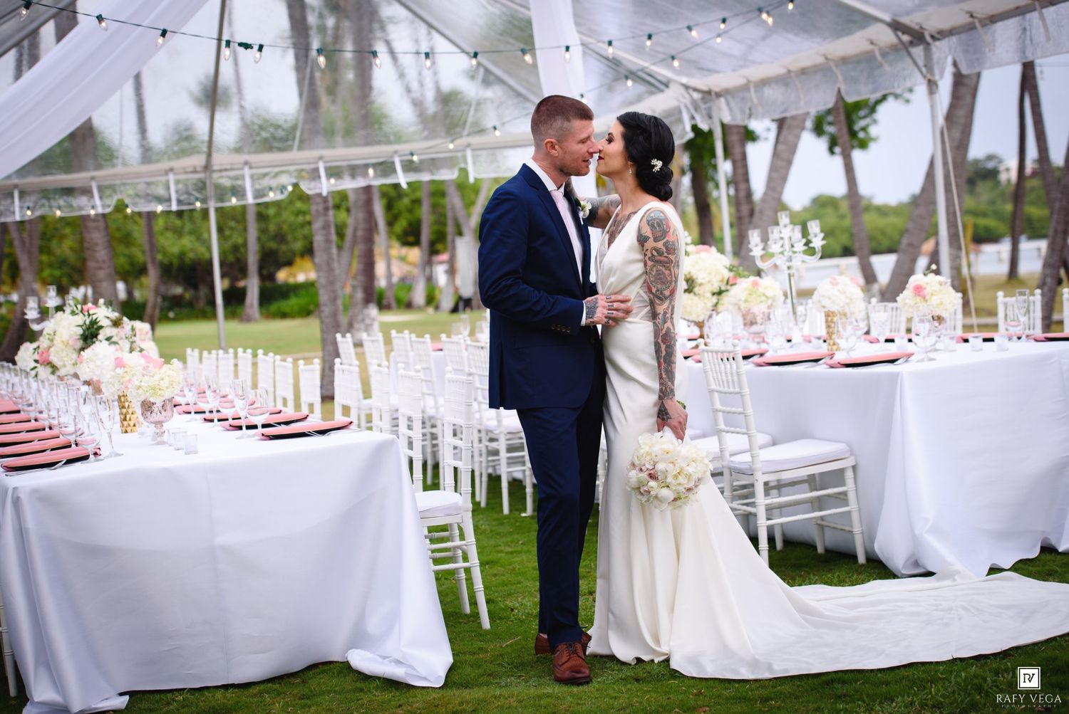Bride and groom share a romantic moment at an elegant outdoor wedding reception under a white tent.