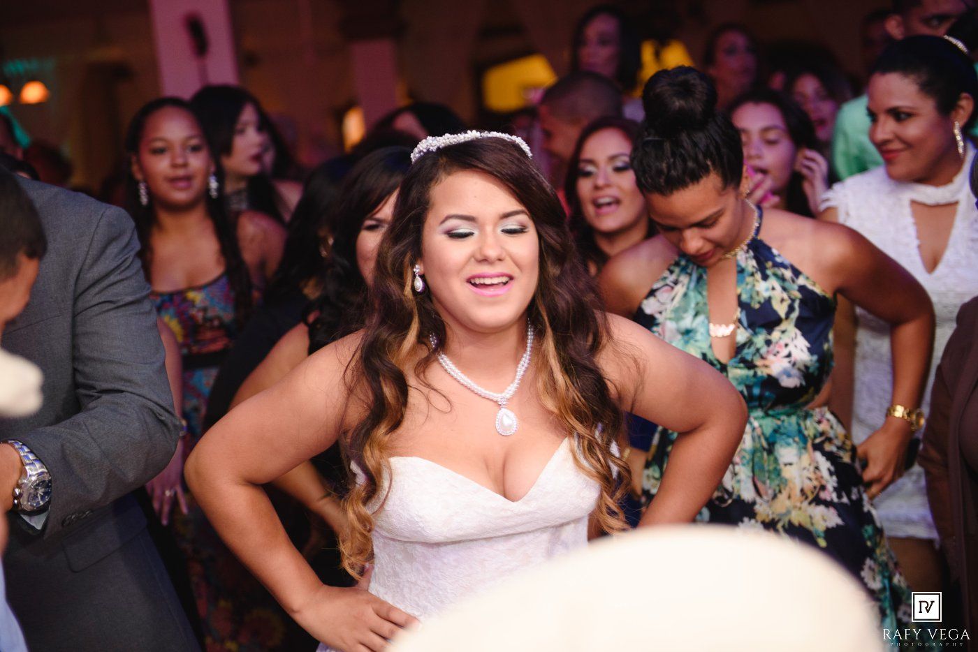 Bride in white wedding dress dancing joyfully at reception party surrounded by guests on the dance floor.