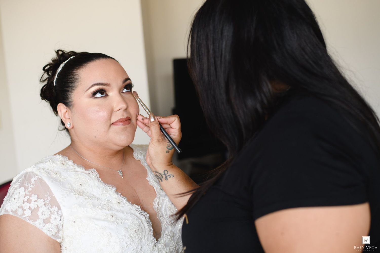 Makeup artist applying eye makeup to a bride in a white lace wedding dress before her wedding ceremony.