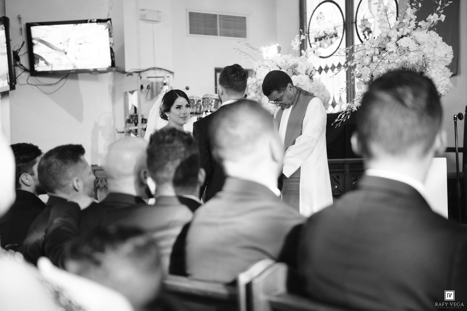 Black and white wedding ceremony photo showing couple at altar with seated guests in elegant venue.
